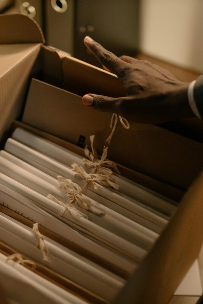 A hand reaches for tied documents inside an archive box, suggesting investigation or record keeping.